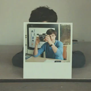 Polaroid photo of polaroid photo sitting on a desk of a young man taking a photo using a polaroid camera