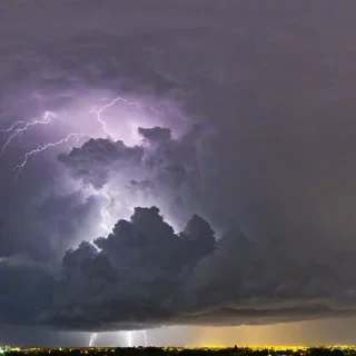Beautiful photograph of of a yellow sky with purple, black, blue, and green thunder clouds with bright flashes visible within the storm to show lightning