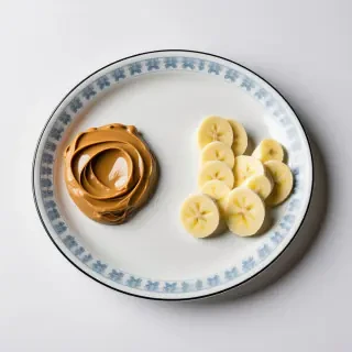 A china platter with a dollop of peanut butter on one side and a pile of banana slices on the other side