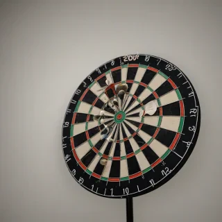 A detailed, high-contrast, full-body view of a traditional dartboard with a single dart embedded in the center of the bullseye, set against a plain white background, with a warm, soft focus lighting, on a plain white background, even lighting 
