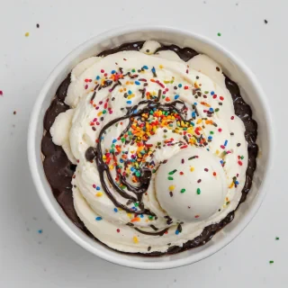 A full-body view of a bowl of creamy vanilla ice cream, topped with a drizzle of rich hot fudge and a generous sprinkle of colorful rainbow sprinkles, on a plain white background, in a photography style with a wide-angle shot and soft, natural lighting, on a plain white background, even lighting