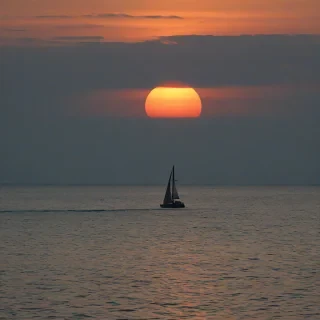 Photograph of a perfect horizon between the teal sea and the sunset sky, the is a sailboat in the center, the orange light creating a silhouette of the boat