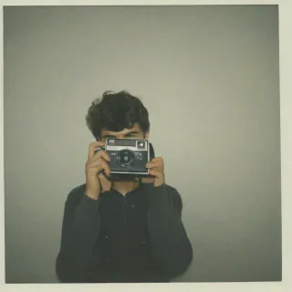 Polaroid photo of a young man taking a photo using a polaroid camera