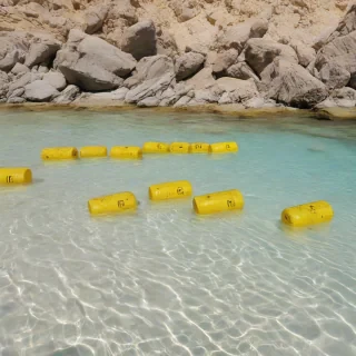 A wide shot of yellow radioactive barrels submerged under clear blue water, surrounded by sand and rocks, with sunlight shining down, full-body view of the barrels, plain white background