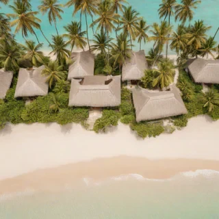 Aerial top-down view of a serene beach with a small hut village seamlessly integrated into the shallow turquoise water, with palm trees and thatched roofs, on a plain white background, impressionist style, wide-angle shot, warm lighting, no humans, no boats, no debris
