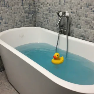 a rubber duck in a bathtub with blue water, no people