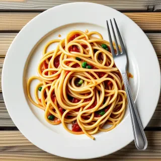A big glass, white plate, covered in spaghetti with a clean fork next to the plate of spaghetti